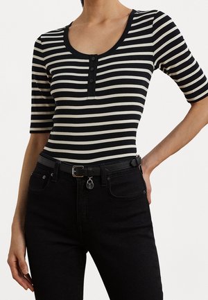 Frau trägt ein schwarz-weiß horizontal gestreiftes Hemd mit Knöpfen und schwarze hoch taillierte Jeans mit schwarzem Gürtel und silberner Schnalle.