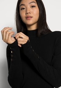 Schwarzes Langarm-Turtleneck aus weichem Stoff, mit Knopfakzenten an den Bündchen und einer taillierten Passform.