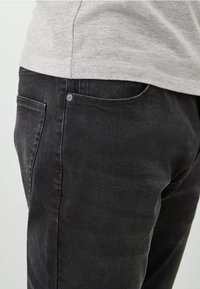 Mustat farkut slim fit -leikkauksella, joissa on klassinen viiden taskun muotoilu, hienovaraiset venytysjäljet ja pieni metallinen nappidetali.