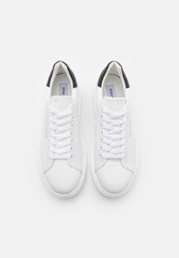 Adidași din piele albă cu o textură netedă, având o capacă neagră la toc, șireturi albe și un design minimalist.