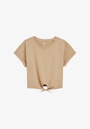 Bežs, īsām piedurknēm t-krekls, kas izgatavots no mīksta kokvilnas auduma. Tam ir apaļš kakla izgriezums un mezglots elements apakšmalā.