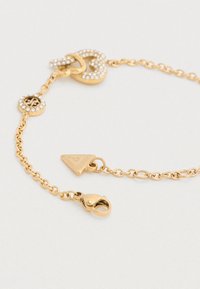 Βραχιόλι αλυσίδας από χρυσό με στρογγυλούς κρίκους, διακοσμητικό κούμπωμα με στρας και τριγωνικό μενταγιόν. Υφή στην επιφάνεια και λαμπερό φινίρισμα.