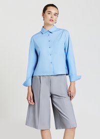 Hellblaues, langärmeliges Hemd mit Knopfleiste und Brusttasche, kombiniert mit grauen, knielangen, maßgeschneiderten Shorts. Glatter Stoff, lockere Passform.