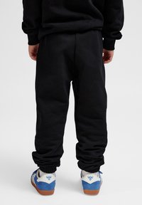 Schwarze Jogginghosen mit elastischen Bündchen und Taillenbund, aus weichem Stoff. Tragen mit blauen und weißen Turnschuhen, die ein markantes Logo aufweisen.