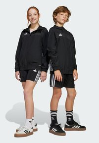 Black athletic jackets with white stripes, paired with black shorts featuring three stripes. Sneakers in black and white with thick soles.