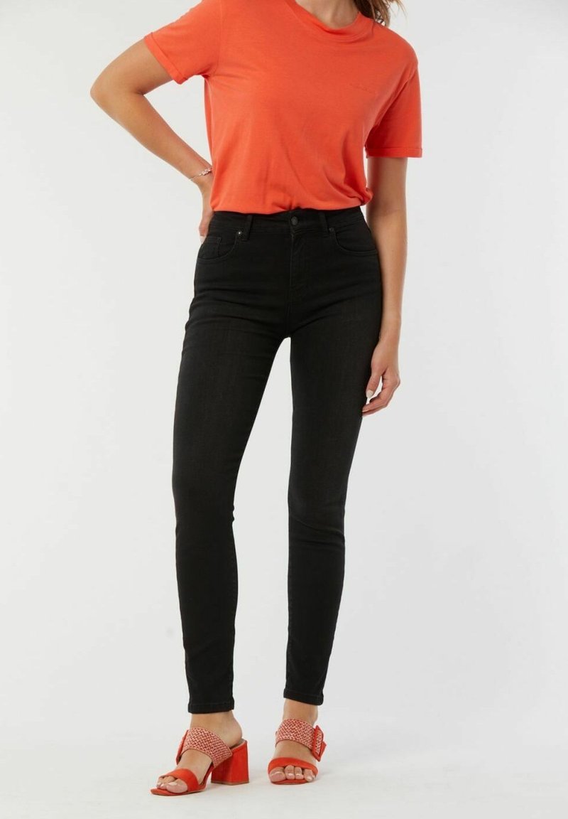 Jeans skinny noirs associés à un t-shirt orange vif et des sandales à talons blocs rouges avec une bride texturée.