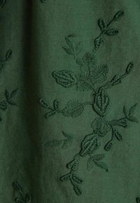 Dunkelgrüner Stoff mit filigraner Stickerei von Blättern und Zweigen in passendem Garn. Glatte Textur mit mattem Finish.