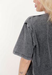 Szara bawełniana koszulka z krótkimi rękawami, luźnym krojem i widocznym detalem przeszyć. Miękka faktura, lekko wyblakły wygląd.