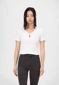 Top bianco a maniche corte con scollatura a goccia, realizzato in tessuto a coste. Abbinato a jeans neri a vita alta. Design minimalista.