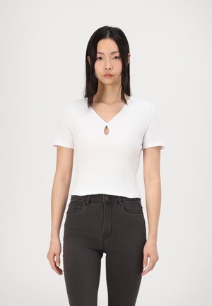 White short-sleeve top with a keyhole neckline, made of ribbed fabric. Paired with high-waisted black jeans. Minimalistic design.