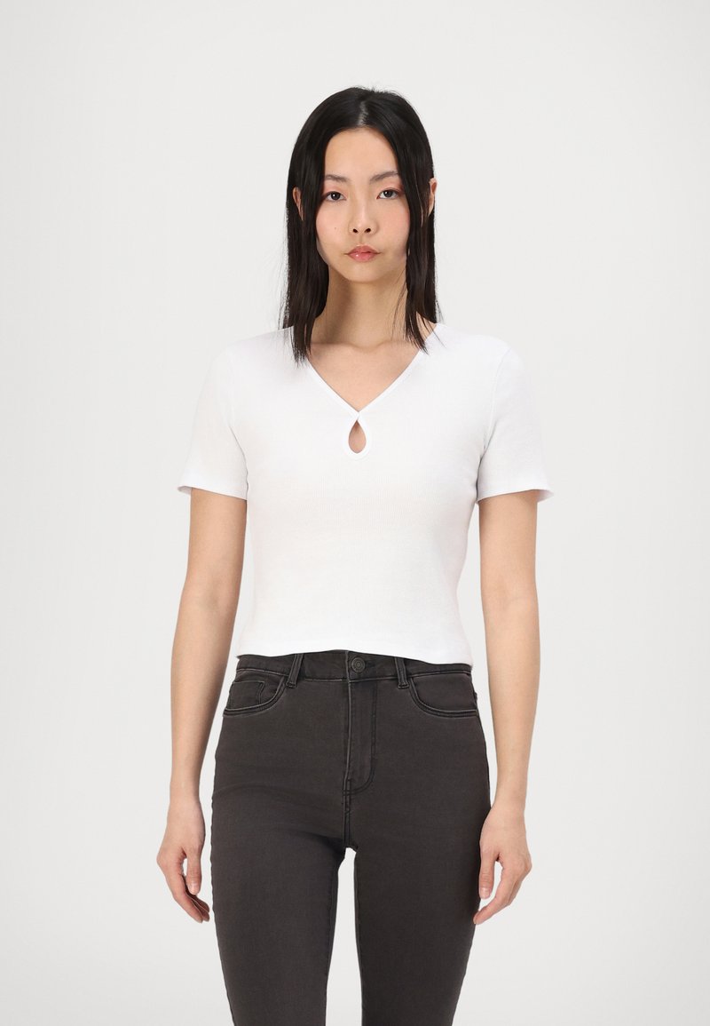 Top bianco a maniche corte con scollatura a goccia, realizzato in tessuto a coste. Abbinato a jeans neri a vita alta. Design minimalista.