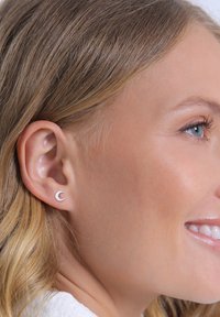 Orecchino a perno a forma di mezzaluna argento esposto su un orecchio. Il design è liscio e minimalista, con una finitura lucida e un delicato splendore.
