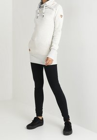 Vaaleanharmaa huppari, jossa on korkea kaulus, nauhat ja teksturoitu sisäosa. Yhdistetty mustiin tiukkoihin farkkuihin ja mustiin tennareihin.