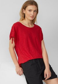 Rode top met korte mouwen, een losse pasvorm, een ronde halslijn en strikdetails aan de mouwen. Gekoeld met zwarte shorts met een gladde textuur.