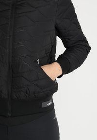 Svart quiltad bombarjacka med dragkedja fram, elastiska muddarna och diagonal sömnad. Inkluderar sidofickor för förvaring.