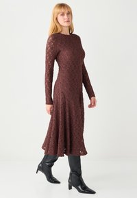 Brązowa sukienka z długim rękawem i koronką, z rozkloszowanym dołem, ozdobiona misternymi wycięciami. Nosi się ją z czarnymi botkami na podeszwie z zaostrzonym noskiem.