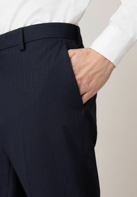 Marineblau gestreifte Hosen mit glatter Textur, ausgestattet mit einer Seitentasche und einer taillierten Passform an der Taille, kombiniert mit einem weißen Hemd.