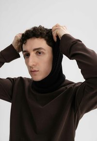 Bruine sweatshirt met een geribbelde zwarte col, slim fit ontwerp, textiele stof, model trekt de hals over hun hoofd.