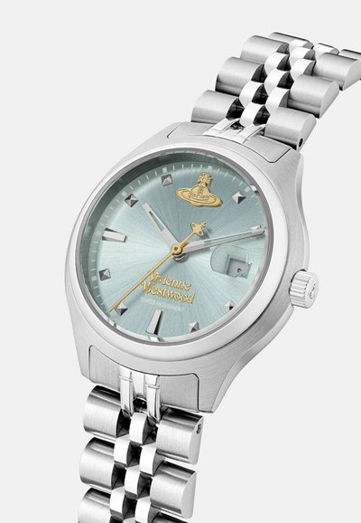 Montre en acier inoxydable argenté avec un cadran texturé bleu clair, des accents dorés, des marqueurs horaires angulaires et un bracelet à maillons.