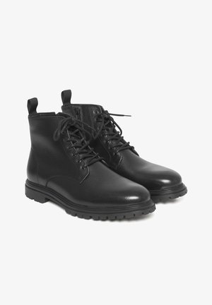 Zwarte leren enkelboots met een gestructureerde afwerking, ronde neus, vetersluiting aan de voorkant en pull tabs, voorzien van een dikke rubberen zool en stikdetails.