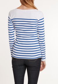 Gestreepte lange mouwen shirt in wit en blauw. Ronde halslijn, zachte katoen stof, slim fit stijl en lange mouwen. Donkere spijkerbroek zichtbaar eronder.