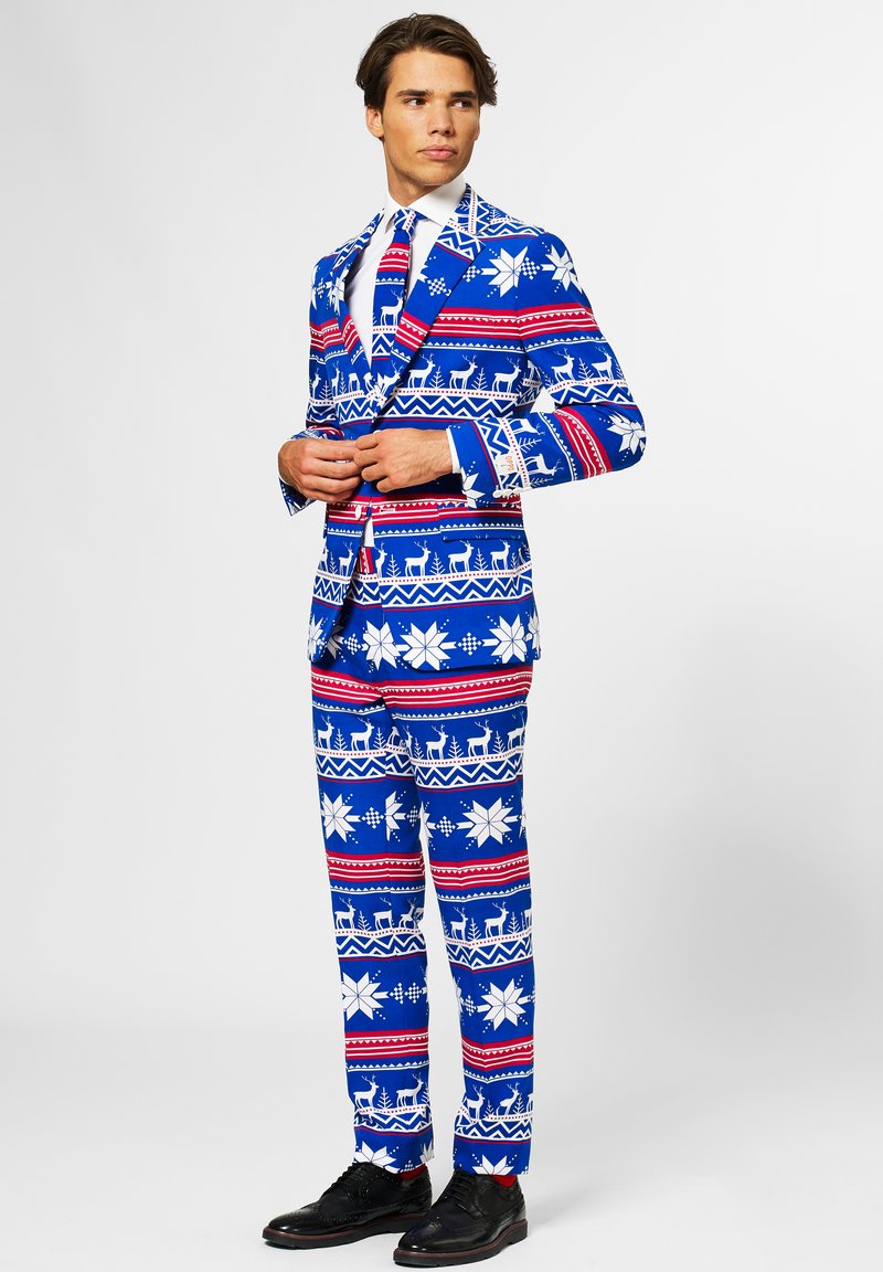 Traje azul con un patrón festivo que incluye copos de nieve blancos, renos y rayas rojas. Incluye una camisa blanca y zapatos negros.
