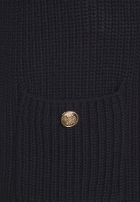 Dunkelblaues geripptes Strickgewebe mit einem goldenen Knopfdetail auf einer Tasche. Die Textur ist weich und dick und hebt die Wärme des Kleidungsstücks hervor.