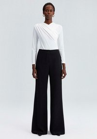 Haut blanc à manches longues avec un design croisé, assorti à un pantalon noir taille haute à jambes larges, présentant un détail à bouton à la taille.