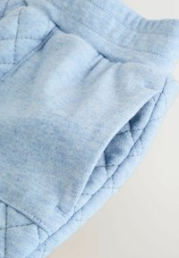Pantaloni jogger in morbido tessuto azzurro chiaro, con dettaglio trapuntato sui lati e cintura elastica. Superficie testurizzata con un delicato motivo mélange.