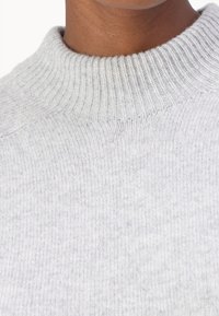 Pull en tricot gris avec un col côtelé et une texture douce. Présente un gros plan du motif subtil du tissu et de sa chaleur.