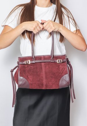 Borsa in suede color bordeaux con dettagli in pelle, manici doppi e tracolla staccabile. Presenta una forma rettangolare elegante e nappine laterali.
