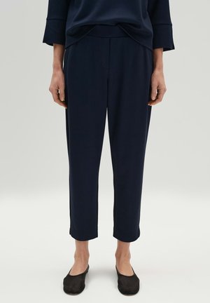 Pantaloni cropped blu navy in un tessuto texturizzato con vita elastica, tasche laterali e cuciture sartoriali, abbinati a ballerine nere.