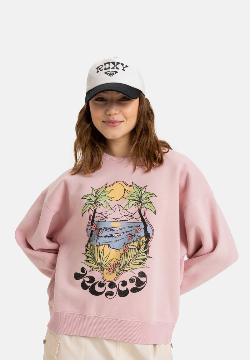 Sweatshirt rose avec un grand motif tropical représentant des palmiers, des montagnes et l'océan. Assorti à une casquette blanche et noire.