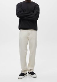 Czarna bluza z długim rękawem w połączeniu z kremowymi prostymi jeansami i czarnymi trampkami z białymi podeszwami, stojąca na jednolitym tle.