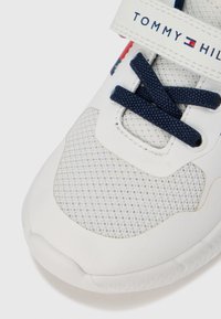 Baskets blanches avec dessus en mesh et synthétique, lacets bleu marine et une bride marquée avec des accents rouges et bleus. Bout arrondi avec semelle texturée.