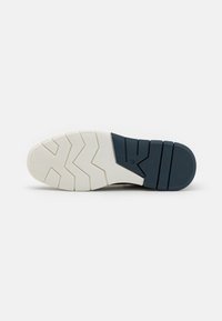Semelle de chaussure de sport avec une semelle en caoutchouc blanche et bleu marine. Présente un motif de bande de roulement en zigzag et des rainures horizontales pour l'adhérence.