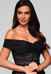 Robe noire décolleté avec un corsage froncé et une superposition transparente à pois. Cheveux longs, accessoires subtils. Texture lisse et fluide.