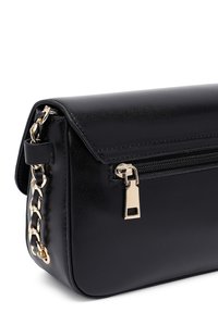 Borsa a tracolla in similpelle nera con chiusura a patta, tracolla in catena dorata e tasca con zip frontale. Texture liscia e forma strutturata.
