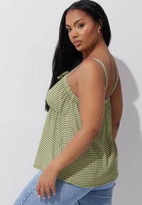 Top de cuadro vichy verde con tirantes ajustables, cintura fruncida y detalle de lazo. La tela es ligera y texturizada, combinada con jeans azules.