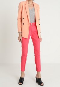 Persikka kaksirivinen bleiseri, harmaa V-kaula-aukko toppi, kirkkaan vaaleanpunaiset kapeat housut ja mustat avonaiset korokepohjakengät. Suorat, muotoonommellut textures.