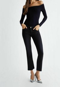 Un jean skinny noir associé à un haut en laine côtelée ajusté à épaules dénudées avec des clous en argent. Le mannequin porte des chaussures à talons hauts argentées.