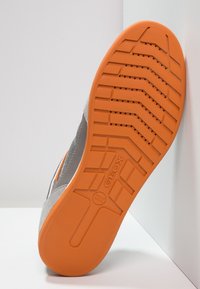 Grå sneakersula med en orange gummiyttersula. Texturerat greppmönster och dräneringshål närvarande. "GEOX"-logotyp synlig.