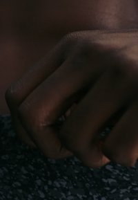 Κλειστό χέρι με σκούρο δέρμα που στηρίζεται σε σκοτεινή, σπορ πασπαλισμένη επιφάνεια με διακριτικό φωτισμό που αναδεικνύει την υφή του δέρματος.