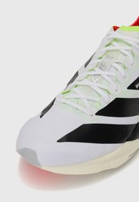 White running shoe with a textured upper, black accents, neon green details on the laces, and a cushioned sole with a red gradient.