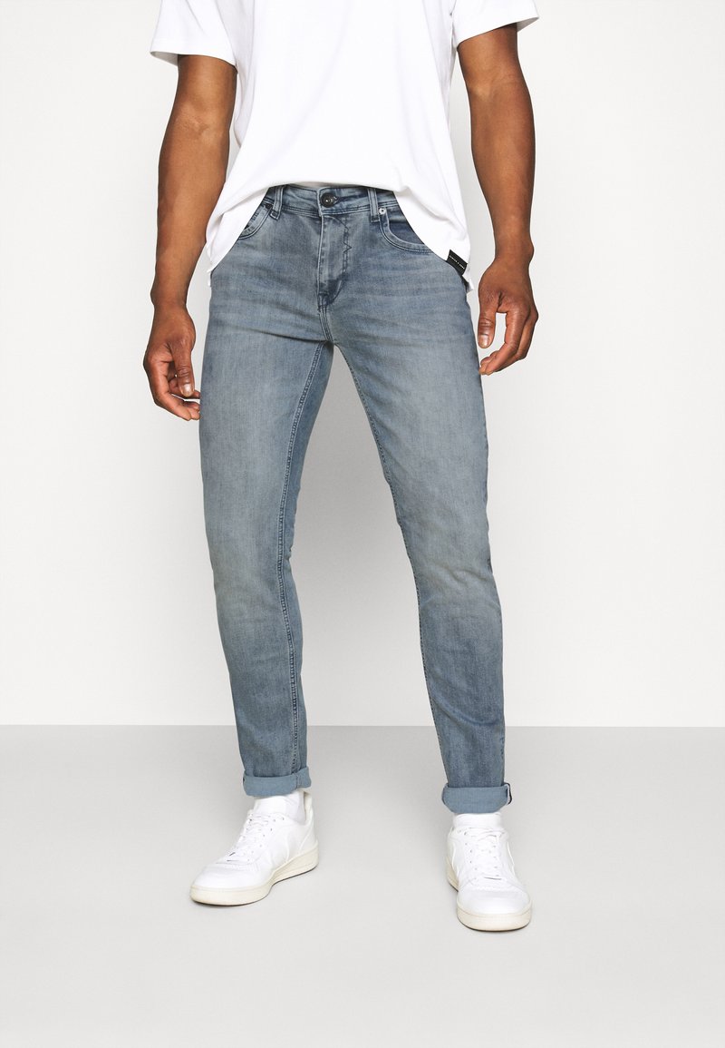 Lichtblauwe spijkerbroek met een slim fit, lichte vervaging en omgeslagen mouwen. Gepaard met witte sneakers, gedragen met een simpel wit t-shirt.