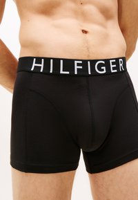 Fekete pamut boxer alsónadrág fekete derékkal, amelyen fehér "HILFIGER" logó látható. Sima textúra és testhezálló kialakítás.