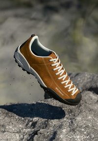 Braunes Wildleder-Kletterschuh mit grauer Gummisohle, weißen Schnürsenkeln und einem gepolsterten blauen Kragen. Verfügt über eine verstärkte Zehenkappe für Haltbarkeit.
