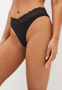 Mustad stringid pitsilise äärega vööjoonel, millel on sile kangas ja minimalistlik disain. Pits lisab tekstuuri ja detaili.