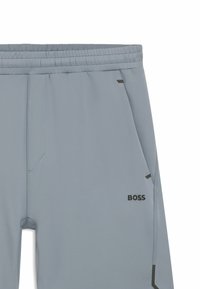 Svetlo sivi atletski hlače z elastičnim pasom, stranskimi žepi in črnimi detajli. Imajo logotip "BOSS" blizu levega spodnjega dela.