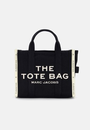Sort lærredstotebag med hvid tekst, der står "THE TOTE BAG MARC JACOBS." Den har solide håndtag og et minimalistisk design.